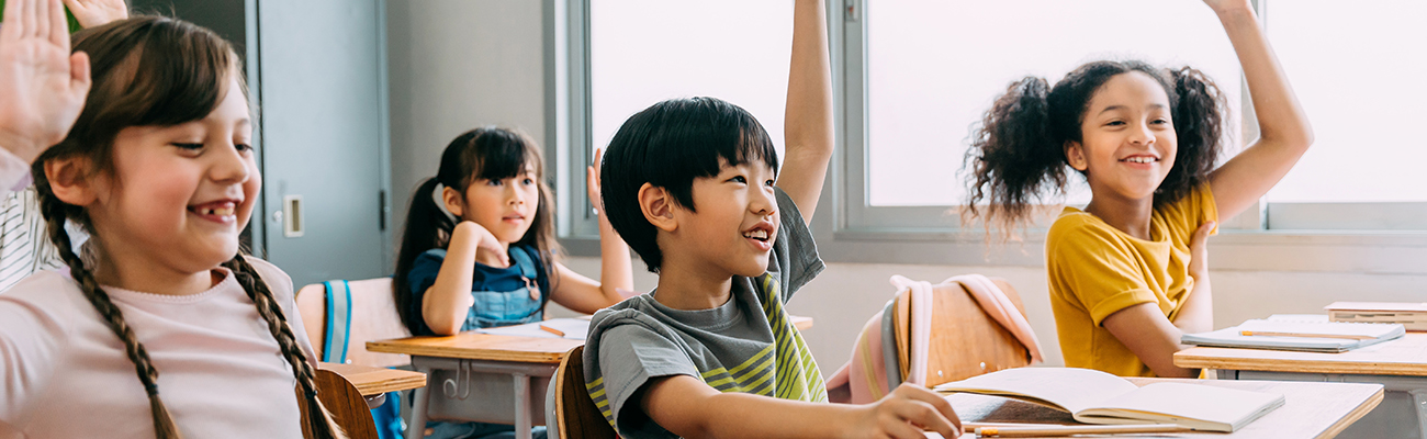 elementary students in class raising hands