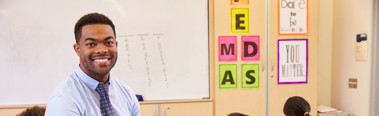 male teacher sitting in classroom smiling