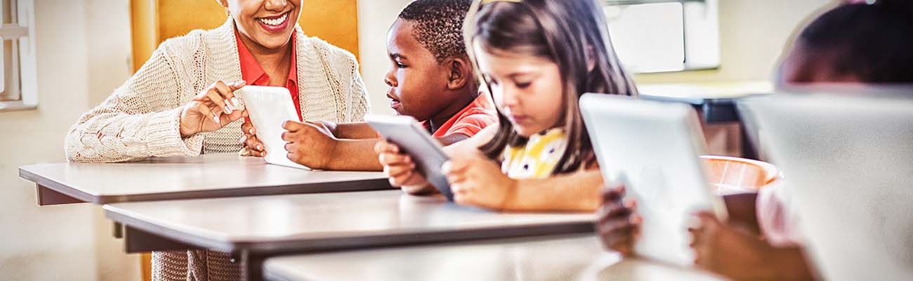 teacher-with-elementary-students-at-desk-using-tablets